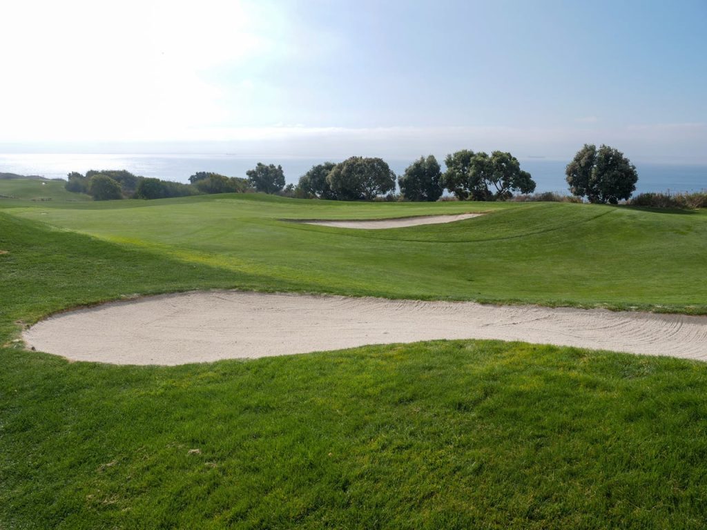 Beautiful golf course with sand trap and ocean view under a clear sky.